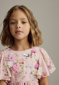Rosa klänning med blommig broderi, volangärmar och ett dekorativt fjärilsnål med paljetter. Mjuk tyg och intrikata detaljer.