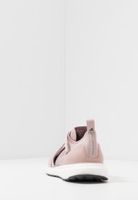 Chaussure de sport rose clair avec dessus en mesh, sangles élastiques réglables et semelle extérieure texturée noire. Présente un intercalaire blanc Boost pour l'amorti.