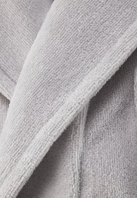 Accappatoio in spugna grigio chiaro con una superficie morbida e strutturata; presenta un colletto sciallato e bordi posteriori sovrapposti.