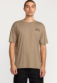 T-shirt di cotone marrone con maniche corte, scollo a girocollo e un piccolo logo stampato sul petto a sinistra. Vestibilità regolare e texture liscia.