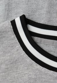 Srebrny materiał w prążki z czarnym i białym kołnierzykiem. Tekstura wydaje się miękka, z delikatnym połyskiem na całej powierzchni materiału.