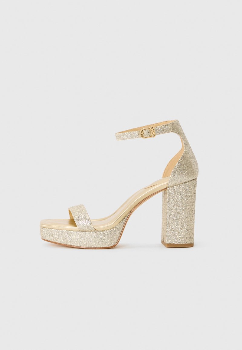 Sandale à talons hauts en plateforme dorée pailletée avec une bride à la cheville et une boucle sur fond blanc.