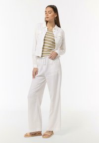 Biała lniana kurtka z dwiema kieszeniami na piersi, zestawiona z beżowo-białą w paski bluzką. Luźne białe spodnie i beżowe sandały dopełniają outfit.