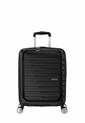 Valigia rigida nera con un design a coste texturizzate, dotata di manico retrattile e quattro ruote per la mobilità. Accentuata da cerniere.
