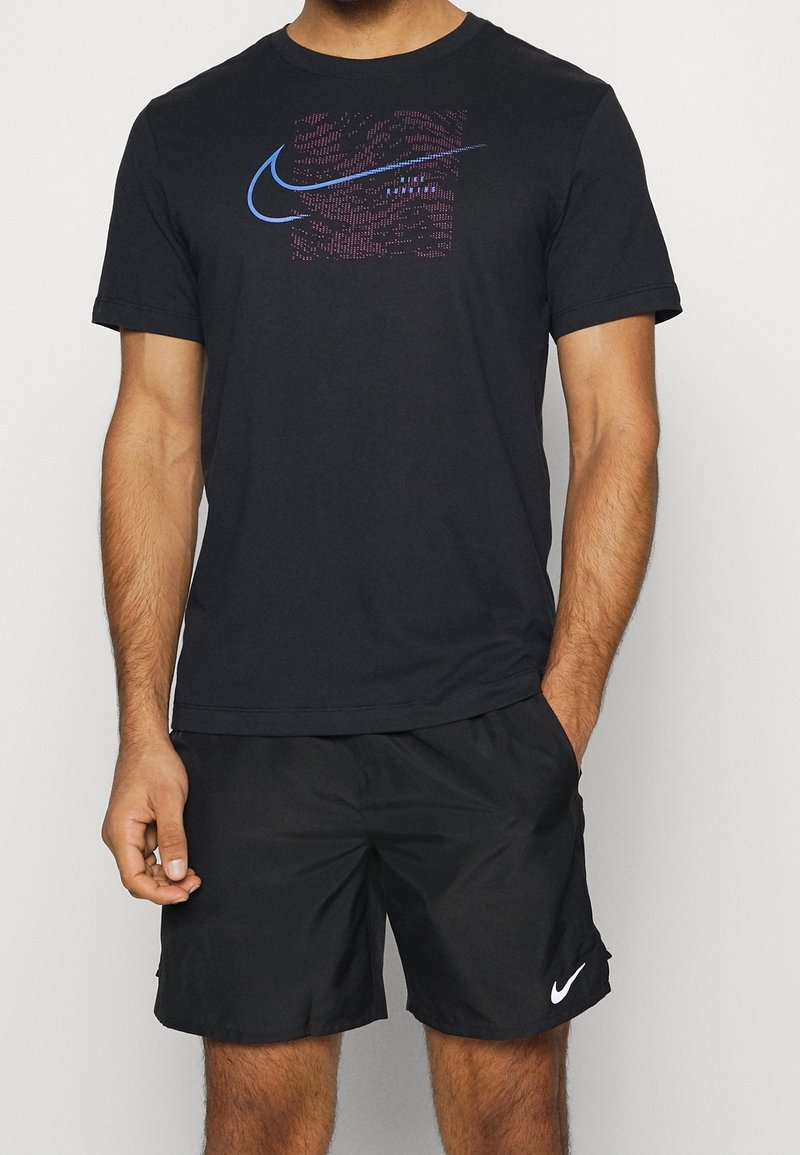 Camiseta negra de Nike con un logotipo gráfico azul y rosa en la parte frontal, combinada con pantalones cortos negros que tienen un logotipo blanco de Nike en el dobladillo inferior.