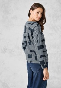 Felpa navy con motivo a righe geometriche bianche, maniche lunghe, collo rotondo e polsini a costine, abbinata a jeans blu.