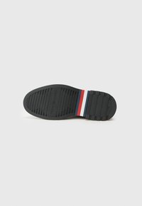 Sort gummisål med struktureret dækmønster; har røde, hvide og blå striber. Brandlogo er præget på sålen.