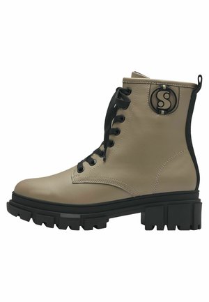 Botas de cuero beige hasta el tobillo con cordones negros, un acento de logo circular y una suela gruesa negra con profundas estrías para tracción.