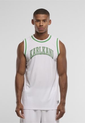 Tânăr purtând un tricou sportiv alb fără mâneci cu margini verzi și textul „KARLKANI”, stând în fața unui fundal gri simplu.