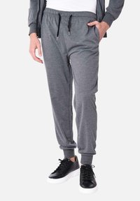 Pantaloni jogger grigi realizzati in tessuto morbido, dotati di vita elasticizzata, cordino regolabile, tasche laterali e polsini aderenti. Abbinati a sneakers nere.