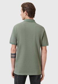 Polo a maniche corte, verde oliva, con una texture morbida, colletto classico e orlo dritto. Presenta dettagli minimi e nessun logo visibile.