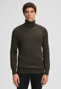 Olivgrüner Rollkragenpullover mit geripptem Stoff und langen Ärmeln, mit taillierter Passform und hohem Kragen. Trägt man über dunklen Jeans.