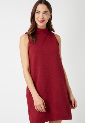 Vestido rojo sin mangas con cuello alto simulado, que presenta una tela texturizada con un patrón sutil. Corte recto, que llega por encima de la rodilla.