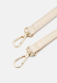 Bracelet en cuir beige avec des clips métalliques de couleur dorée à chaque extrémité. Présente une texture lisse et des coutures soignées le long du bord.