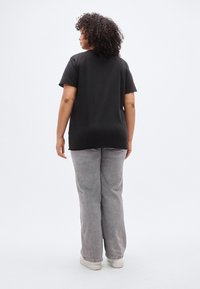 Černé bavlněné tričko s krátkými rukávy, volného střihu, kombinované s světle šedými džínovými kalhotami. Oba oděvy jsou jednoduché a bez ozdob.