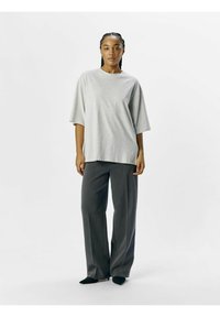 Lysegrå oversized t-shirt med korte ærmer, parret med mørkegrå plisserede bukser med brede ben og spidse sorte sko.