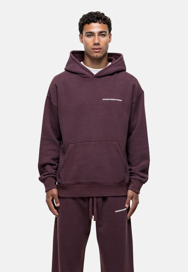Bordowy, kapturowy sweatshirt wykonany z miękkiego materiału, z kieszenią z przodu i białym napisem "GOODFORNOTHING" na lewej części klatki piersiowej.
