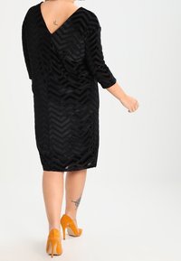 Black dress featuring a chevron pattern, three-quarter sleeves, and a V-back, paired with orange high-heeled shoes. Smooth texture.