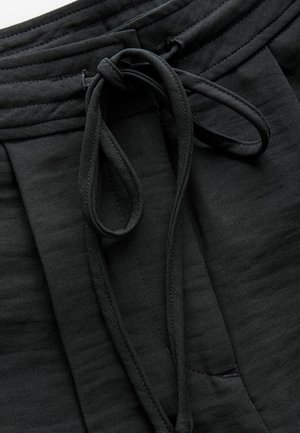 Pantaloni jogging neri realizzati in tessuto morbido, dotati di vita con coulisse, una texture sottile e dettagli con tasche laterali.