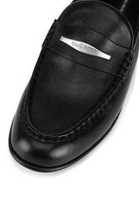 Čierne kožené mokasíny s hladkým povrchom, prešitým dizajnom a strieborným akcentom so značkou "Gino Rossi" na vrchu.