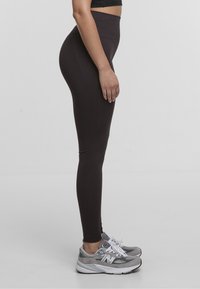 Leggings neri a vita alta realizzati in tessuto elasticizzato, con una texture liscia. Abbinate a scarpe da ginnastica grigie con dettagli bianchi.