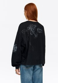 Sudadera negra de gran tamaño con rosas texturizadas y detalles brillantes en las mangas y la parte trasera, con un detalle gráfico de texto.