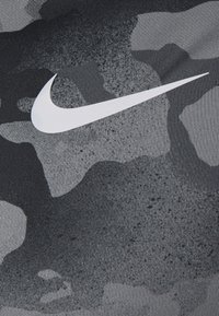 Svart och grå kamouflageväv med en slät yta, som har en framträdande vit Nike-logotyp på den övre sidan.