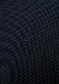 Black textured fabric featuring a subtle grid pattern with an embossed ampersand logo, creating a distinct surface detail.