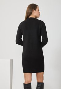 Schwarzes Strickkleid mit langen Ärmeln, rundem Ausschnitt und geripptem Saum. Verfügt über eine glatte Textur und eine figurbetonte Silhouette.
