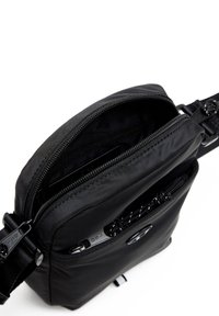 Svart nylon crossbody-väska med en framficka med dragkedja, justerbar rem och slät yta. Har två fack med dragkedja för förvaring.