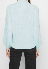 Ljusblå stickad tröja med hög krage, överdimensionerade ärmar och ribbade mudd. Har ett strukturerat mönster på baksidan.