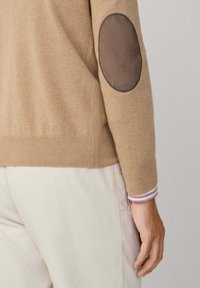 Maglione beige in maglia con toppe in suede marrone sui gomiti, polsini a coste con strisce multicolori e corpo testurizzato.