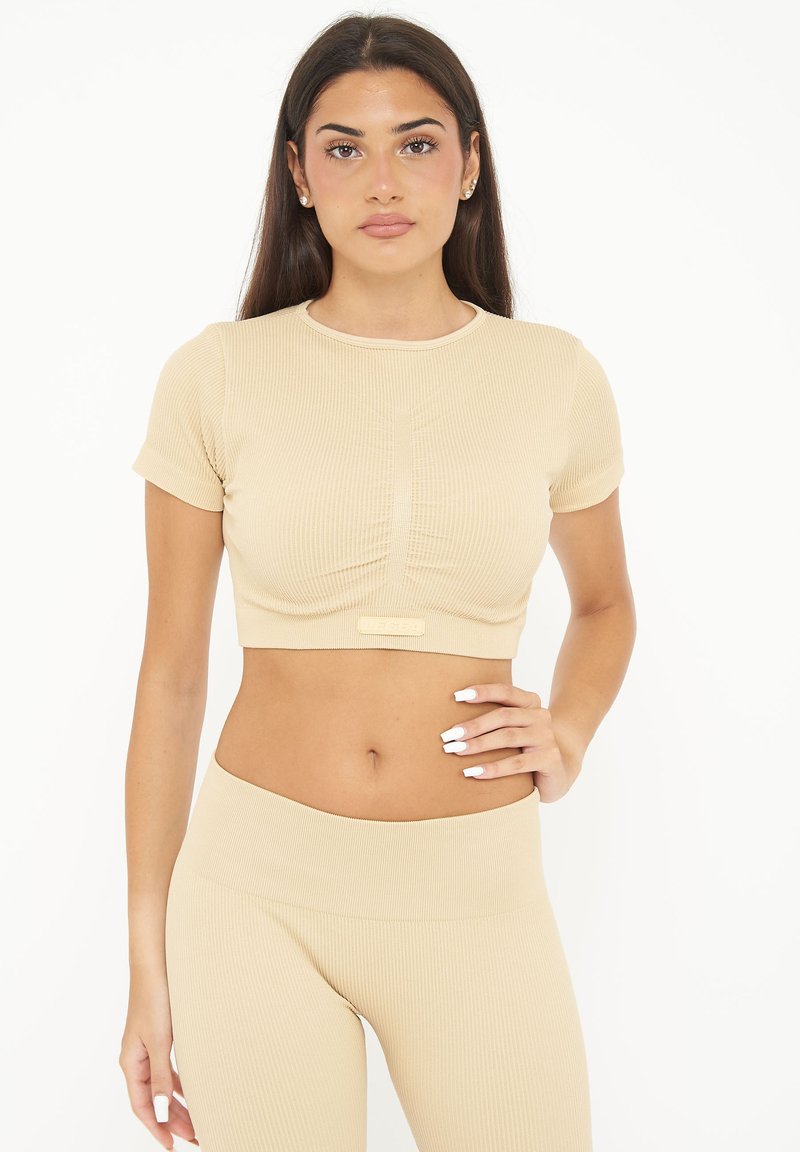 Beige ribbet crop top med kortærmer, der har et tætsiddende design, front ruching-detalje og et logo aksent i sømmen.