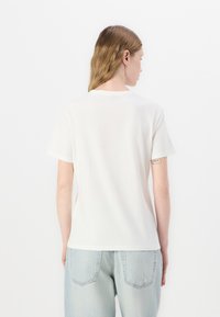 Tricou alb cu mâneci scurte, fabricat din bumbac moale, cu un guler clasic rotund; purtat cu blugi din denim de culoare albastru deschis. Textură netedă, design minimal.