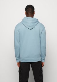 Ljusblå hoodie med avslappnad passform, känguruficka och dragsko i huvan. Tröjan har ribbade ärmslut och nederkant, tillverkad av mjukt tyg.