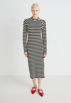 Black and cream striped ribbed dress with long sleeves, a high neckline, and decorative buttons on the shoulder. Red pointed flats worn.