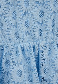 Világoskék csipkés anyag virágmintával, finoman részletezett margaréta mintákkal és texturált réteggel. A csipkén összegyűrt szegélydísz található.