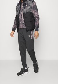 Svart vadderad väst över en marmorerad mörklila sweatshirt, kombinerad med grå joggers. Svarta sportskor kompletterar looken.