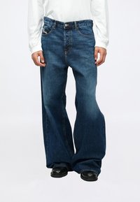 Mėlynos džinsinės kelnes su plačia, laisva kelnės kojomis, aukšta juosmens linija, penkiais kišenėmis ir kontrastine siūle.