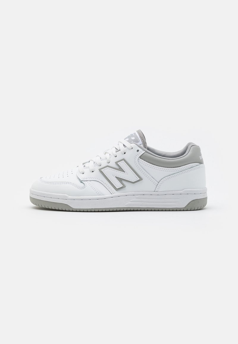 Baskets basses New Balance blanches et grises avec lacets, bout perforé et semelle texturée sur fond blanc uni.