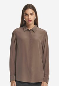 Brun, långärmad blus med krage, slät textur och knäppt front. Har raka linjer och en subtil glans.