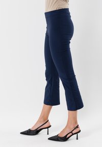 Pantaloni cropped blu navy con una texture liscia e un design aderente. Abbinati a scarpe con tacco a scomparsa nere dotate di punta affusolata e tacco basso.