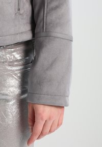 Harmaa mokkajakun hiha, jossa on sileä rakenne. Sisältää siistin muotoilun ja saumat, sekä metallinhohtoisen hopeahameen, joka näkyy alapuolella.