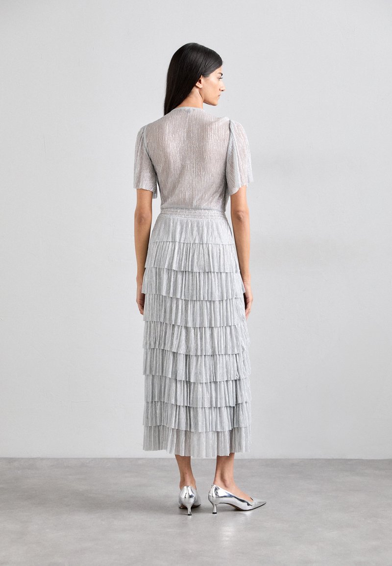 Silver pleated dress with short puff sleeves, featuring a tiered skirt. Paired with sleek silver heeled shoes.