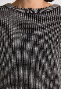 Knitted sweater in black and white, featuring a ribbed texture, round neckline, and a small logo detail on the front.