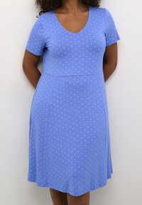 En blå kortærmet kjole med hvide prikker, der har en V-udskæring og en A-line silhuet, lavet af et glat, strækbart stof.