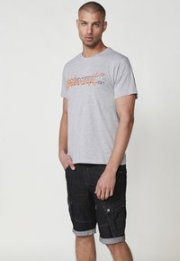 Gray short-sleeve T-shirt with graphic print in orange and black, paired with dark denim cargo shorts featuring rolled cuffs and pockets.