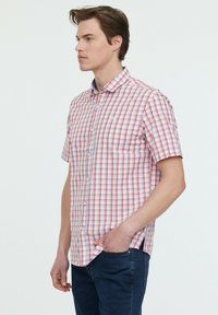 Chemise à manches courtes en motif carreaux rouges et blancs, avec un col boutonné et tissu léger. Associée à un jean noir.