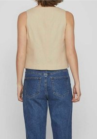 Béžový tílko bez rukávů se čtvercovým výstřihem, doplněné vysokými modrými džínami s kapsami na zadní straně a volným střihem.
