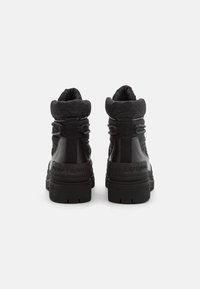 Par de botas de tobillo negras de Tommy Hilfiger con cuellos acolchados de quilt y suelas de goma gruesas, mostradas desde la parte trasera sobre un fondo blanco.